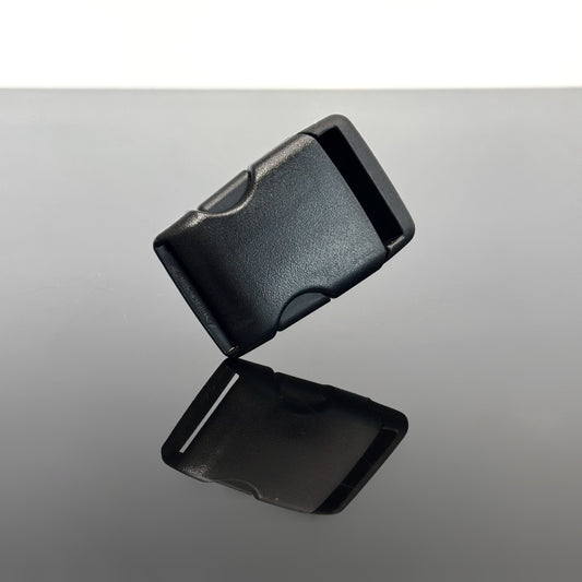 A black plastic buckle with a textured finish, shown floating above a reflective gray surface.