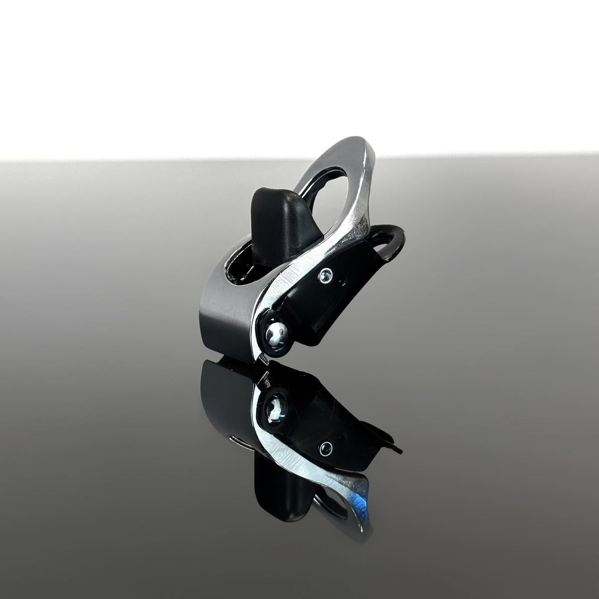 A silver harness ratchet displayed on a reflective dark surface against a white background.