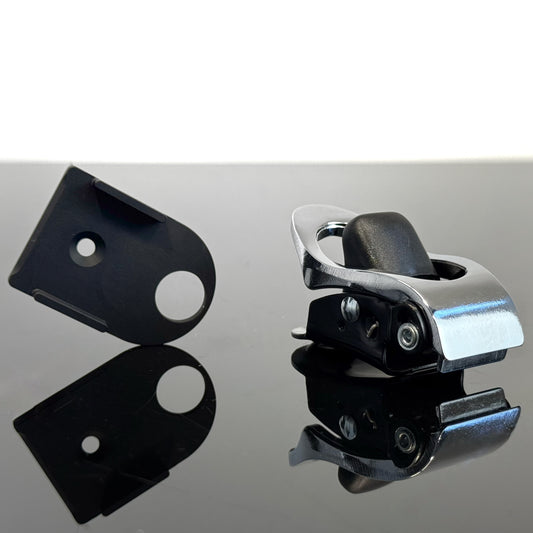 A black aluminum ratchet plate for mounting ratchets and a silver harness  ratchet, displayed on a reflective dark surface against a white background.