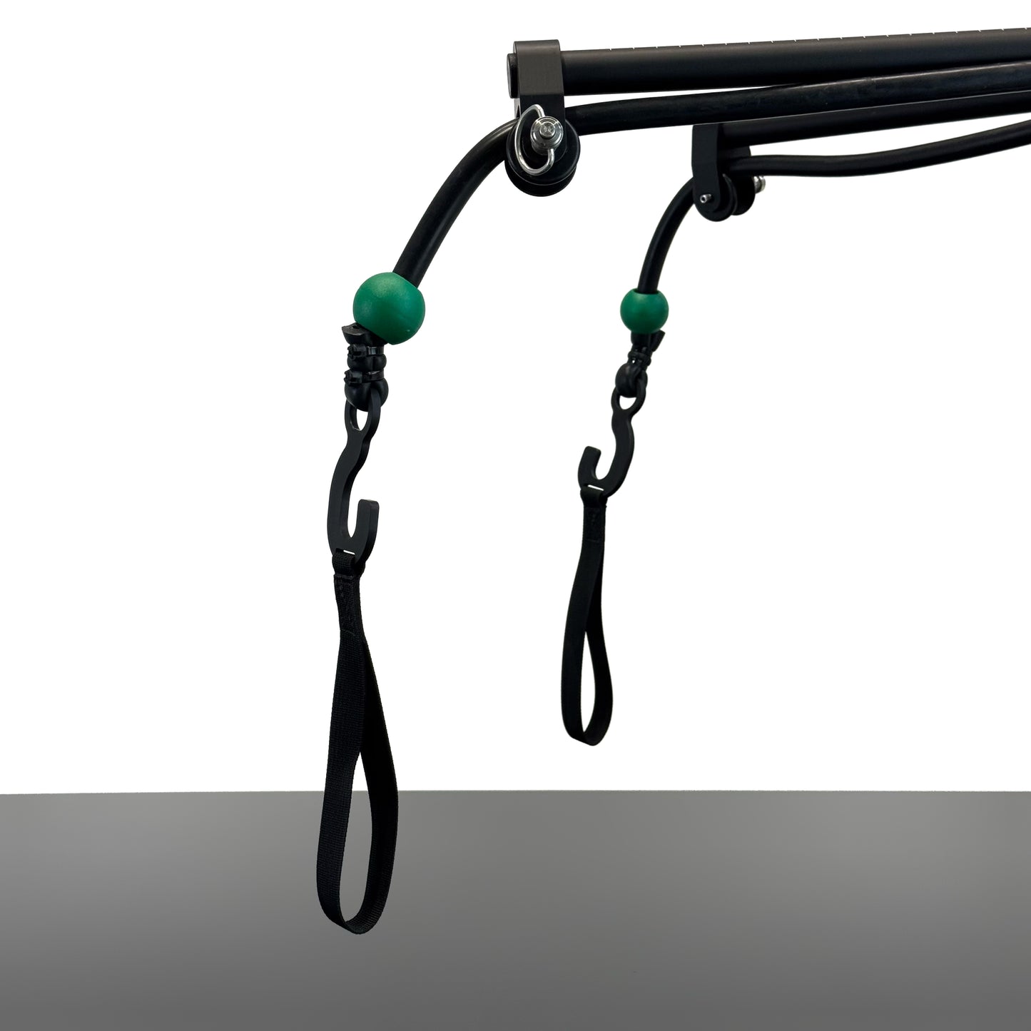 Black metal SlingShot camera mount arms ending with two rubber elastics knotted with green rubber stoppers and metal hooks with loops hanging at the end, shown against a white background above a grey table.