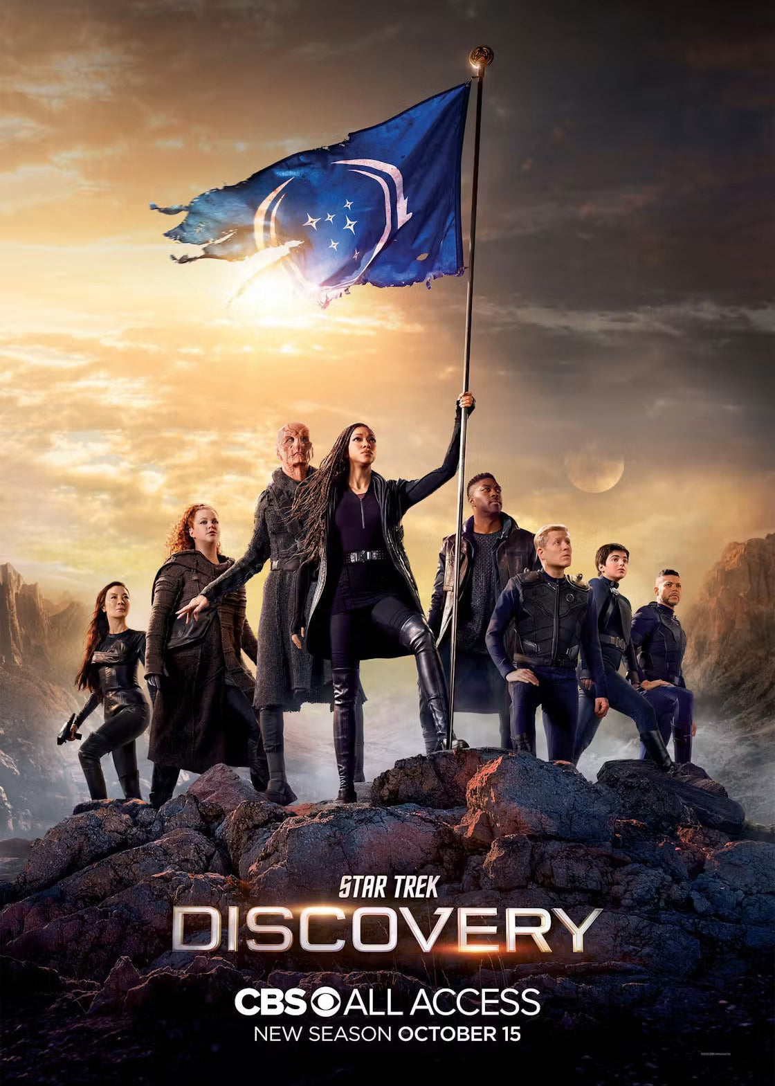 Promotional poster for 'Star Trek Discovery' season 3 featuring the crew standing on dark rocks under a dramatic sunset sky, holding a tattered blue Discovery flag. 